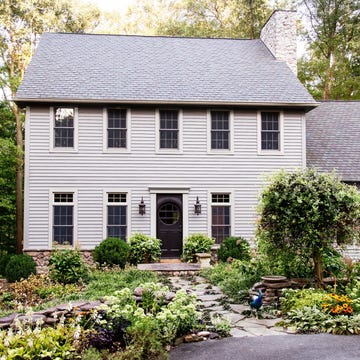 A two-story house surrounded by lush gardens and trees.